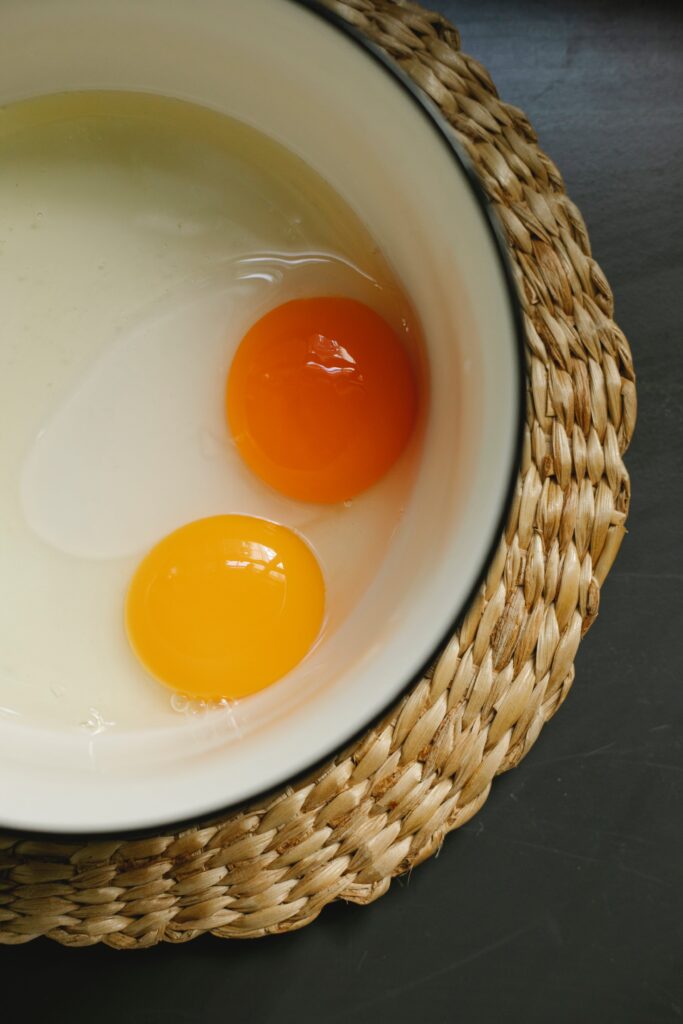 Raw eggs in enamel bowl placed on rattan placemat in morning